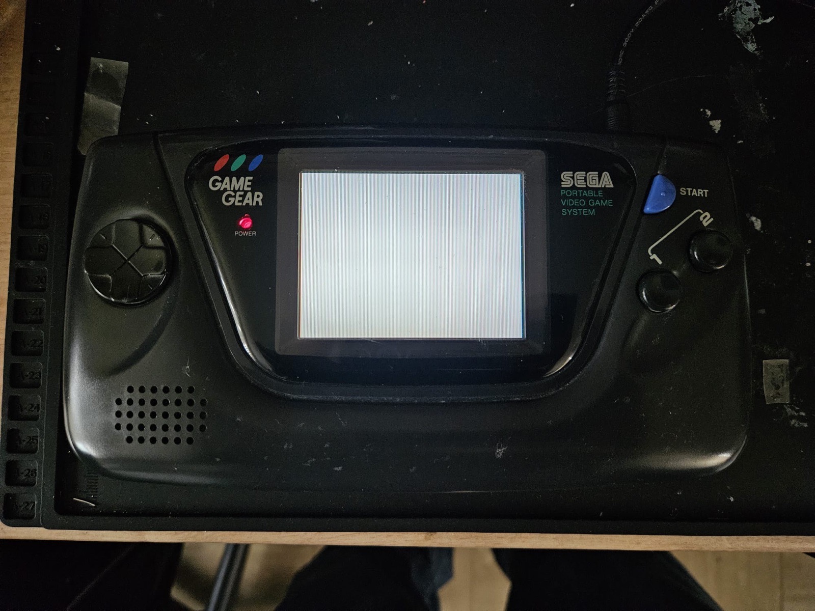 The repaired Sega Game Gear powered on at the Hark Tech bench, power LED lit and the original screen evenly backlit