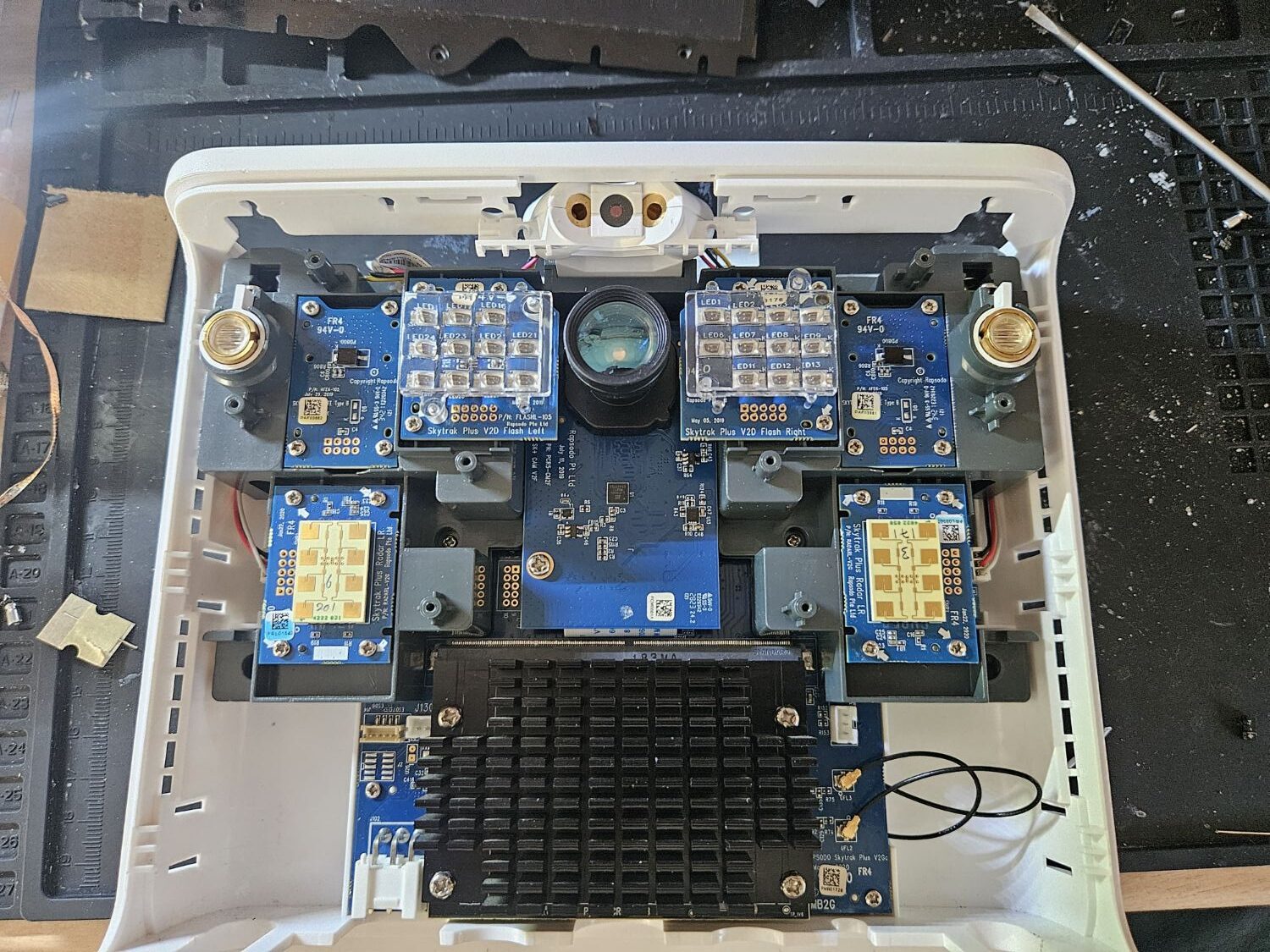 A SkyTrak+ launch monitor stripped open on the bench, showing the camera, two flash LED boards, two radar boards and the main board under its heatsink