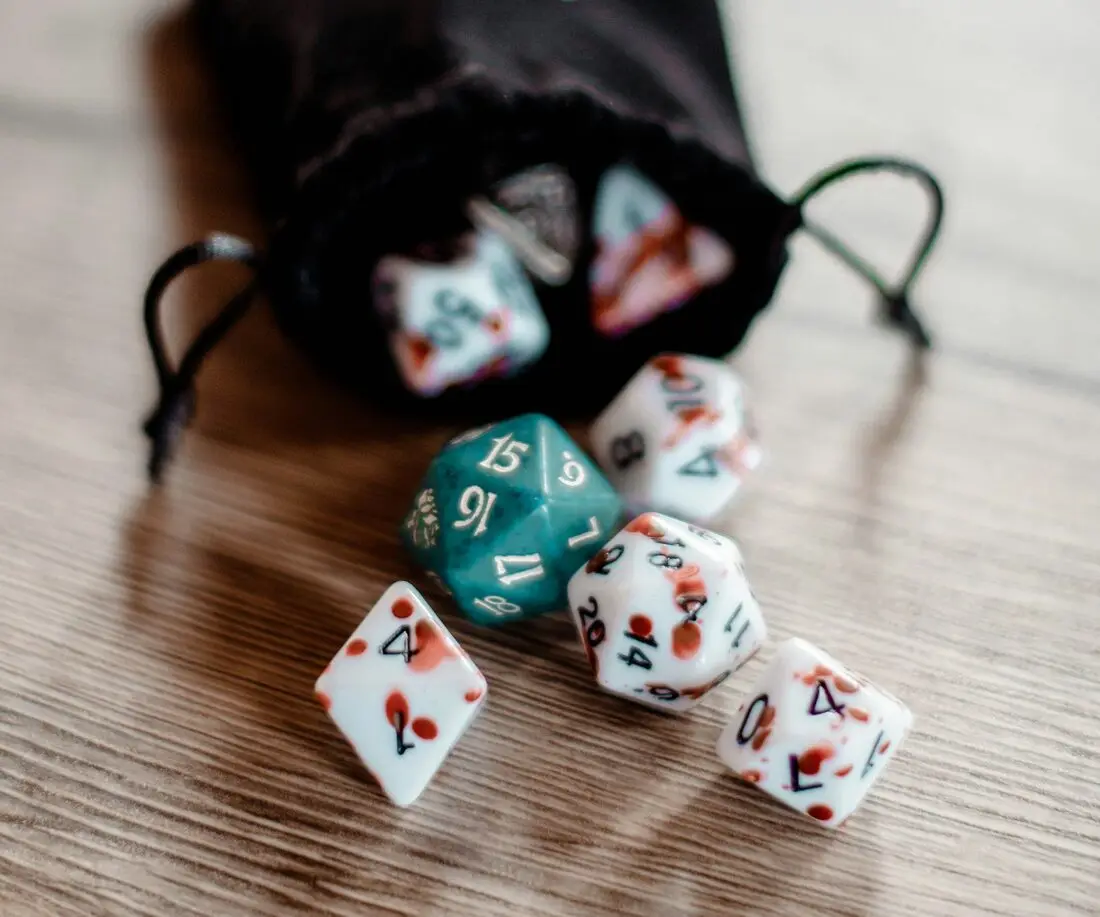 Polyhedral dice spilling out of a drawstring bag onto a wooden table