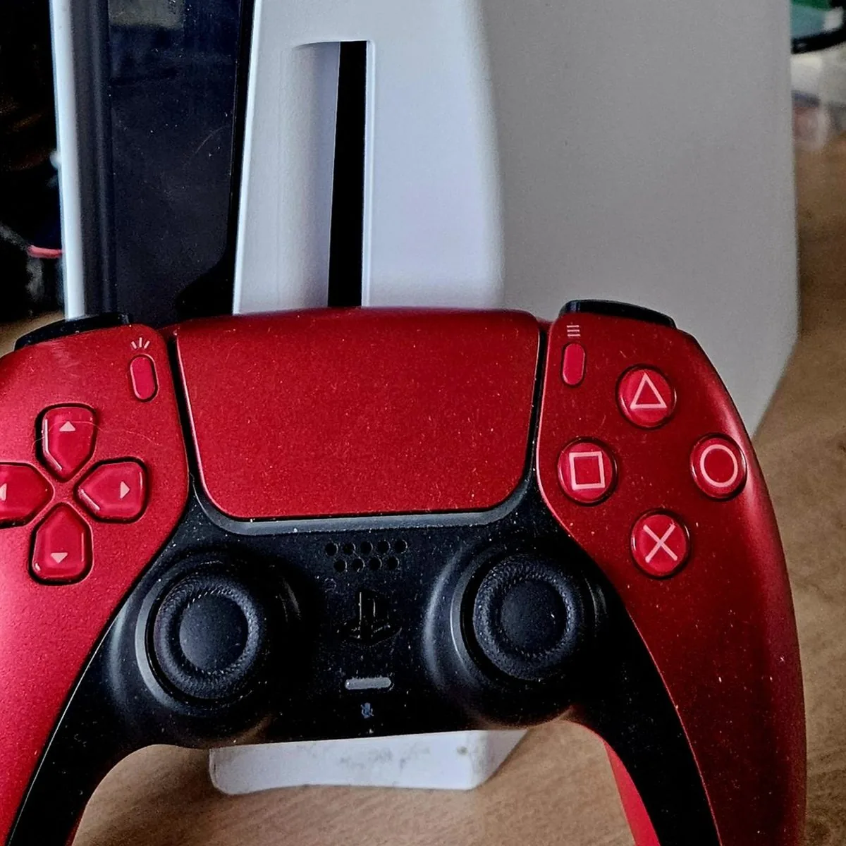 Red PlayStation DualSense controller in front of a PlayStation 5