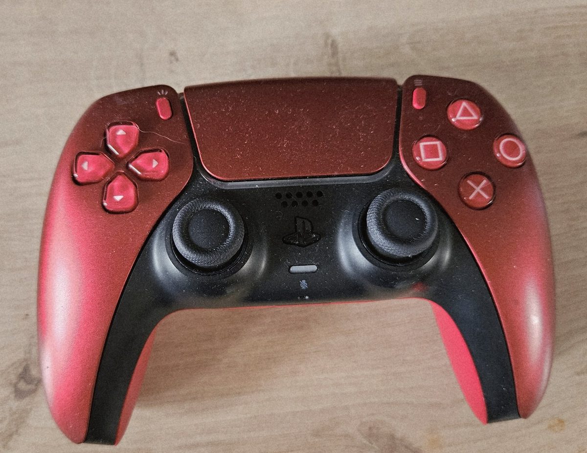 Red Sony DualSense PS5 controller on the Hark Tech workshop bench, top-down view