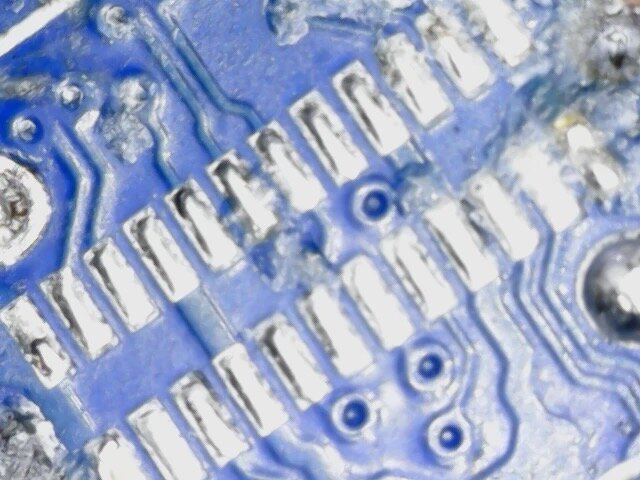 The SkyTrak+ board under a microscope after the old USB-C socket was removed, showing two intact rows of pads