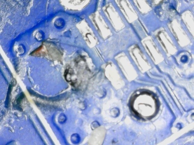A small crater beside the USB-C pads where one of the socket&rsquo;s anchor legs tore out of the board